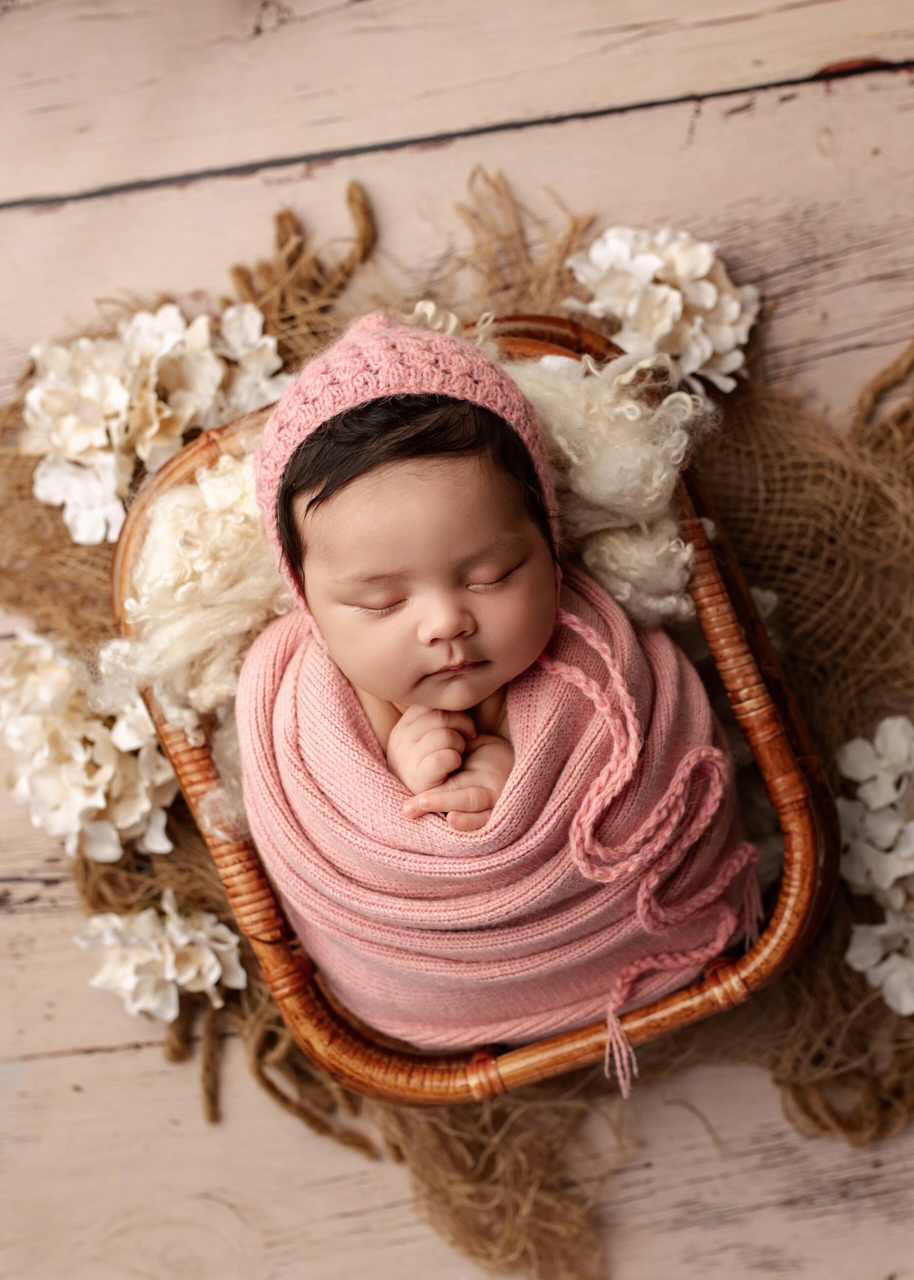 baby girl wrapped in pink in a basket surrounded by cream florals in Prince George, BC. APNPI award winning photographer