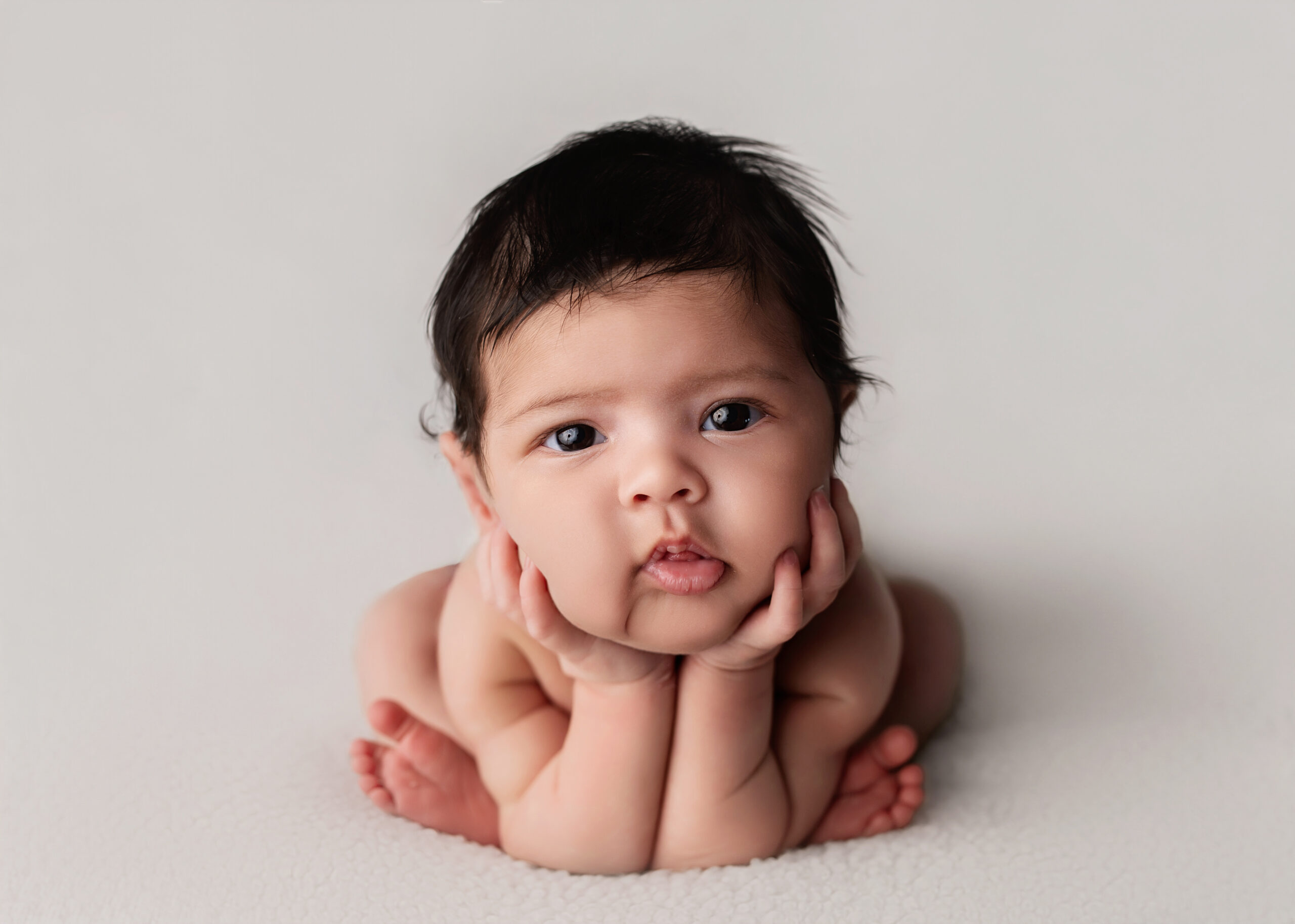 BAby gitl with lots of hair, posed with her chin on her hands in a Froggy Pose.